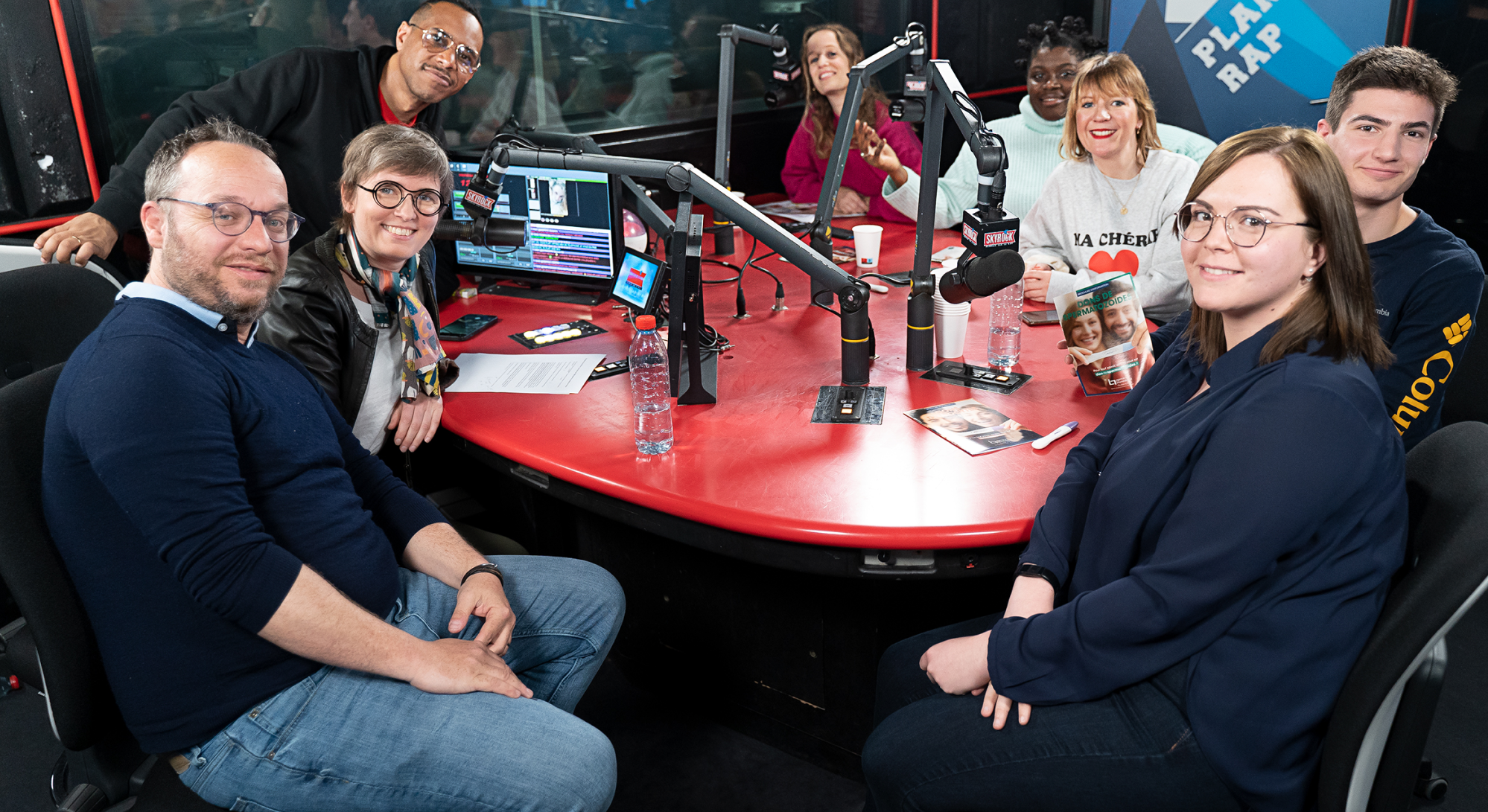 8 personnes avec des micros autour d'une table enregistrent une émission sur Skyrock