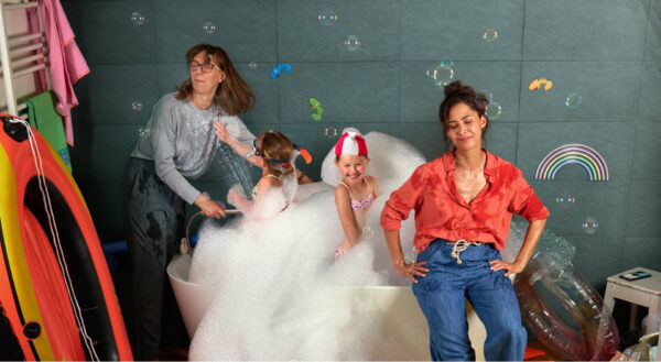 Deux femmes sont dans la salle de bain avec leurs enfants qui ont trop fait moussé la baignoire.