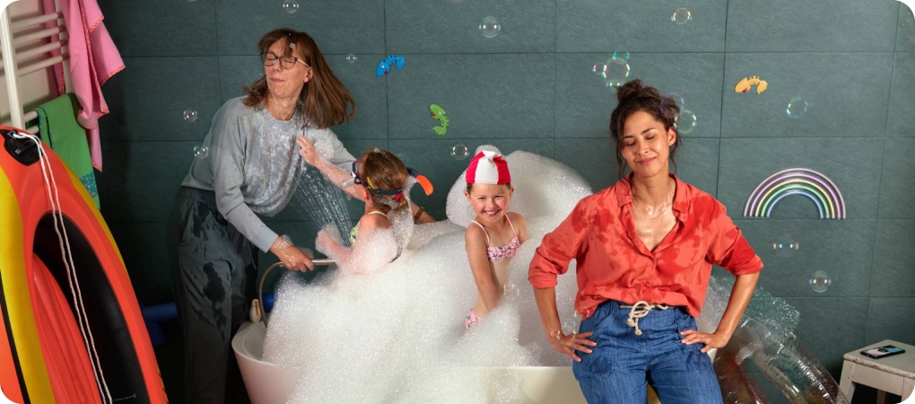 Deux femmes sont dans la salle de bain avec leurs enfants qui ont trop fait moussé la baignoire.